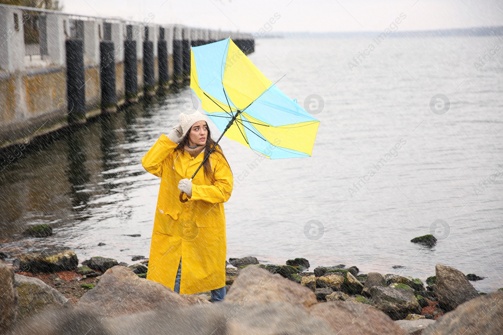 Photo of Woman in yellow raincoat with umbrella caught in gust of wind near river