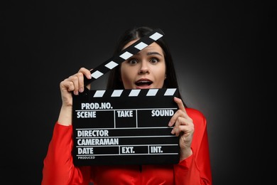 Emotional actress with clapperboard on black background. Film industry
