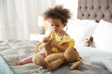 Cute African American child imagining herself as doctor while playing with stethoscope and toy bunny at home