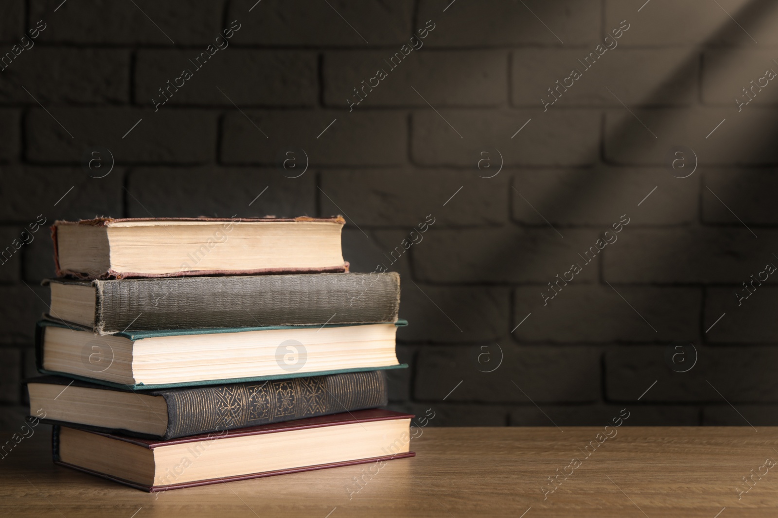 Image of Stack of old hardcover books on wooden table near brick wall, space for text