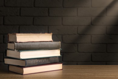 Stack of old hardcover books on wooden table near brick wall, space for text