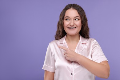 Photo of Smiling woman with braces pointing at something against violet background, space for text