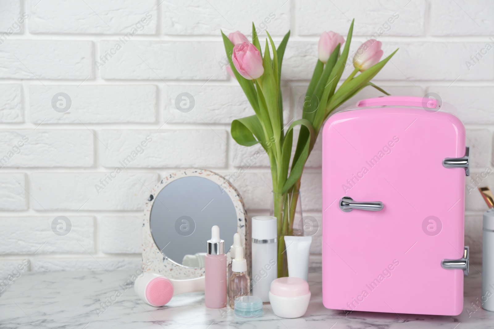 Photo of Cosmetic refrigerator and skin care products on white marble table