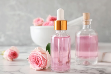 Photo of Bottle of essential oil and rose on marble table