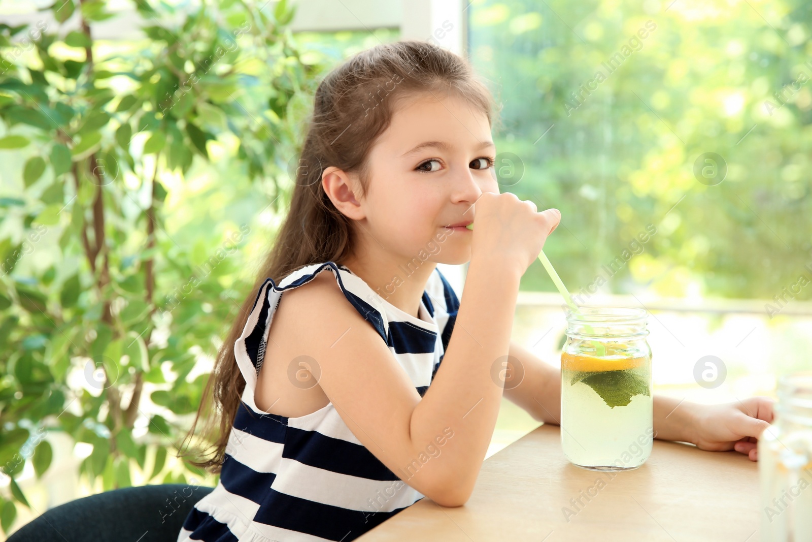 Photo of Little girl with natural lemonade at table indoors