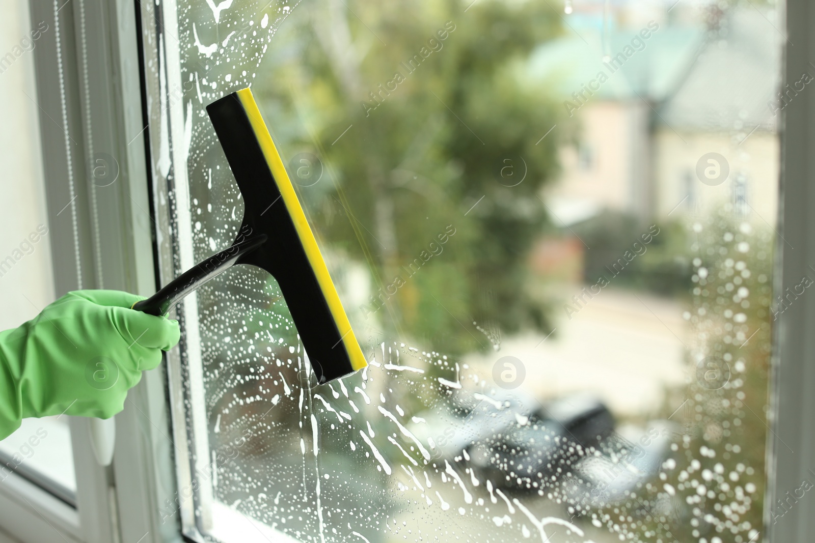 Photo of Woman cleaning glass with squeegee indoors, closeup