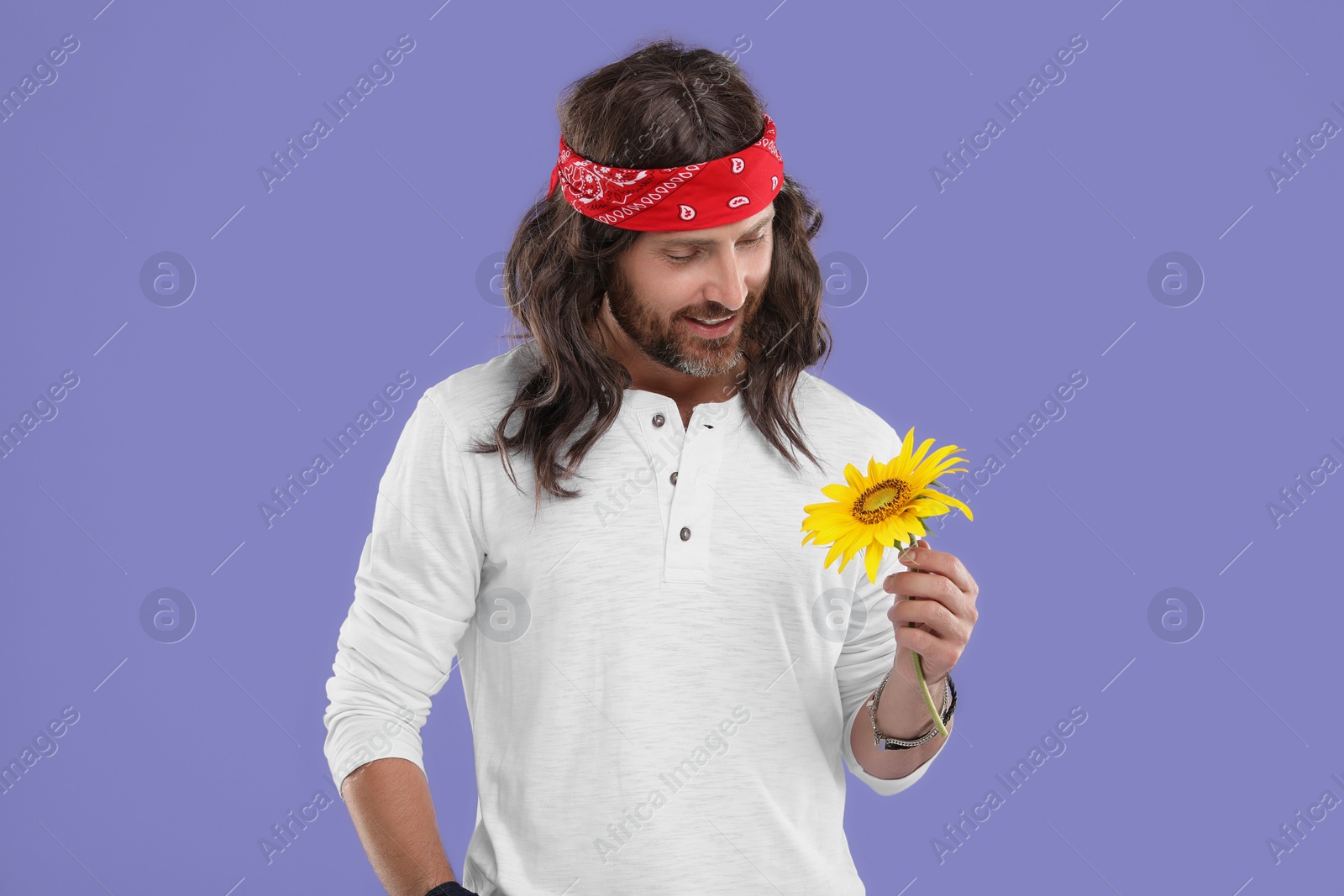 Photo of Stylish hippie man with sunflower on violet background