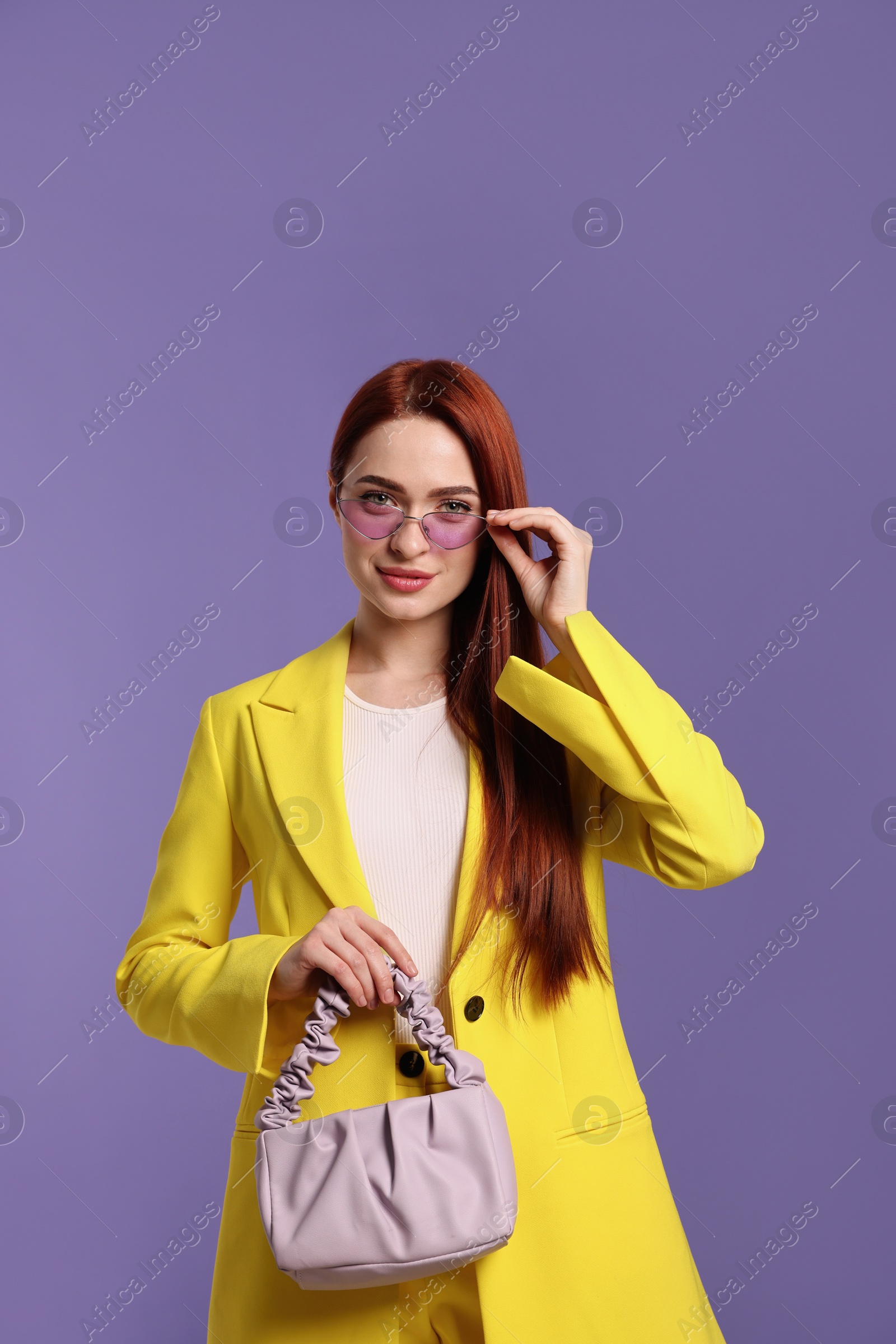 Photo of Stylish woman with red dyed hair and bag on purple background