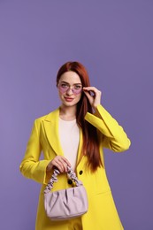 Photo of Stylish woman with red dyed hair and bag on purple background