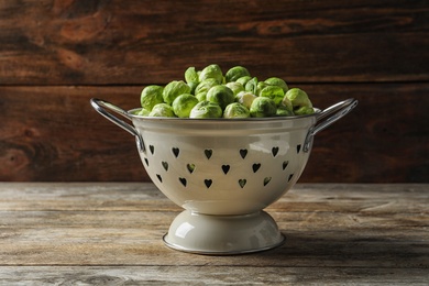 Photo of Colander with Brussels sprouts on wooden background