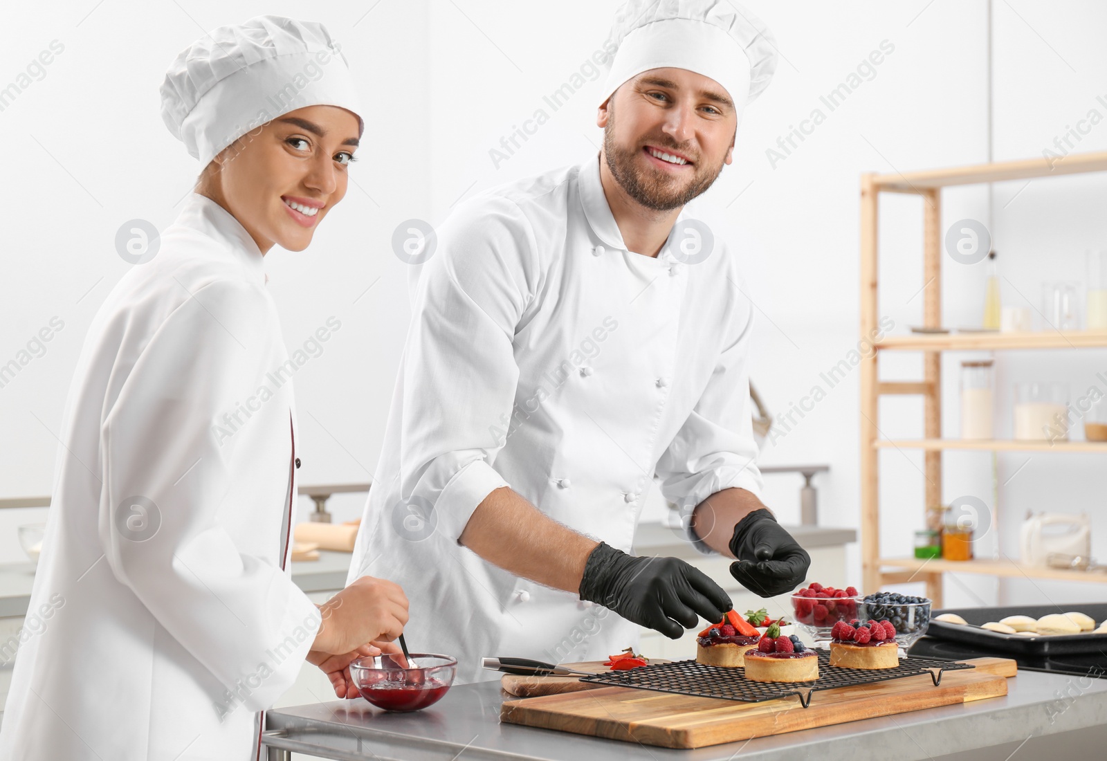 Photo of Pastry chefs preparing desserts at table in kitchen