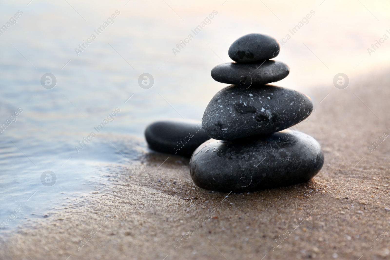 Photo of Dark stones on sand near sea at sunset, space for text. Zen concept