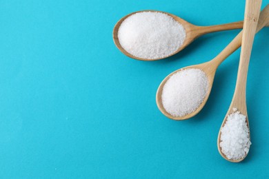 Photo of Organic white salt in spoons on light blue background, flat lay