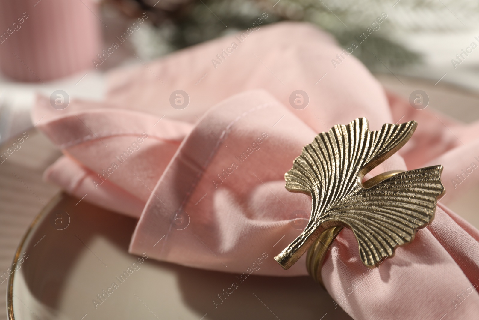 Photo of Pink fabric napkin with beautiful decorative ring for table setting on plate, closeup