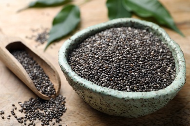 Bowl and scoop with chia seeds on wooden table, closeup