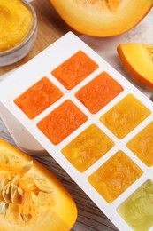 Photo of Different purees in ice cube tray ready for freezing and fresh pumpkin on table