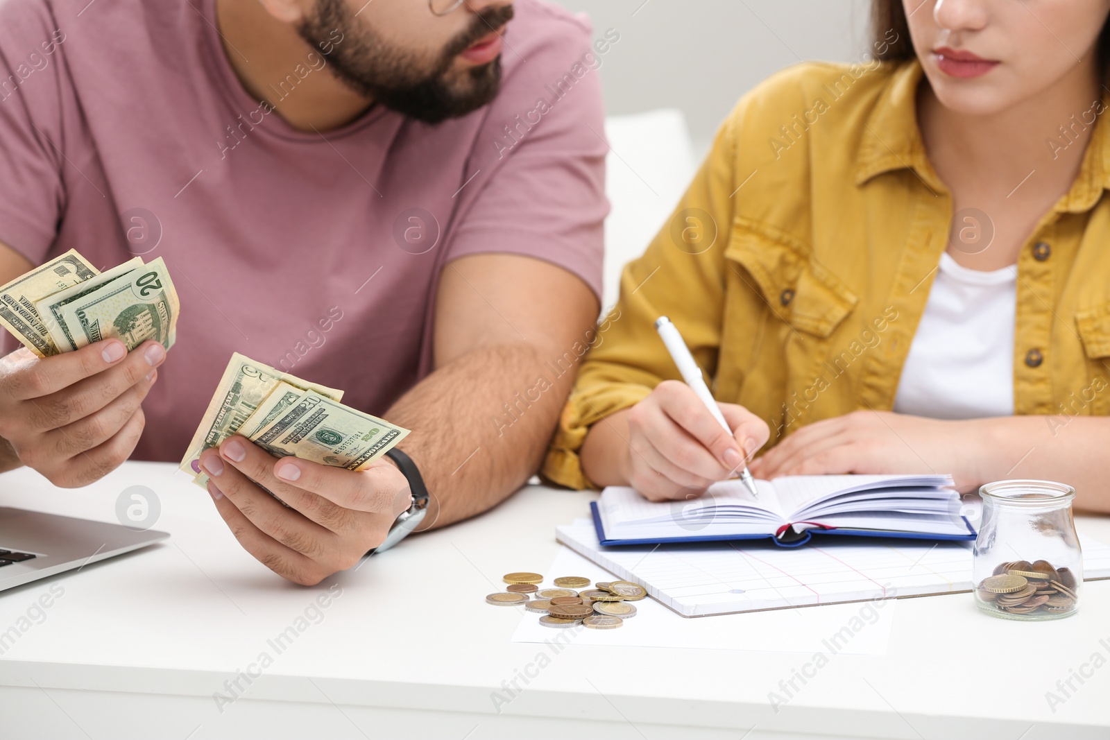 Photo of Young couple counting money at white table indoors, closeup