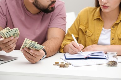 Photo of Young couple counting money at white table indoors, closeup