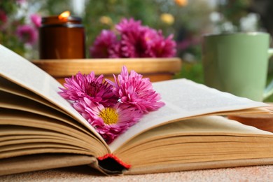 Photo of Book with chrysanthemum flowers as bookmark on beige textured table, closeup
