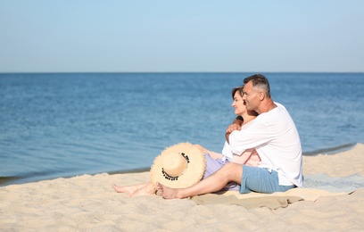 Happy mature couple sitting together at beach on sunny day