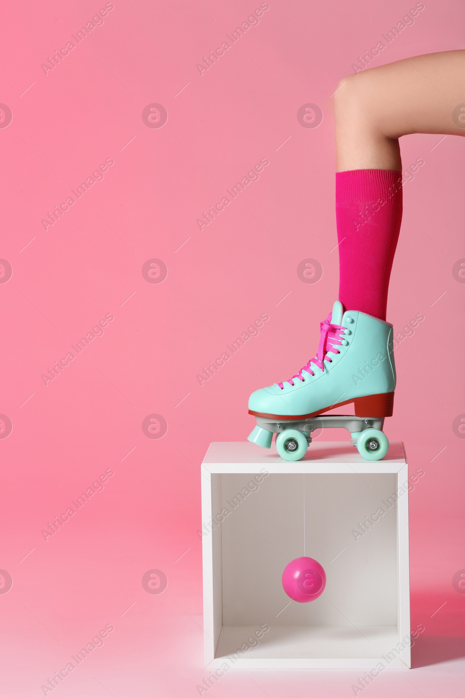 Photo of Woman wearing vintage roller skate and storage cube with ball against color background, closeup