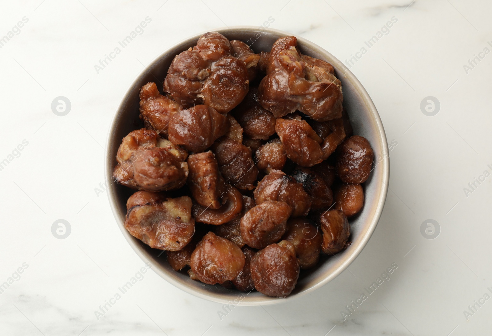 Photo of Roasted edible sweet chestnuts in bowl on white marble table, top view