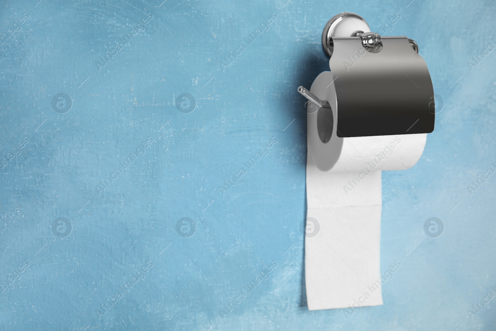Photo of Toilet paper holder with roll on color background. Space for text