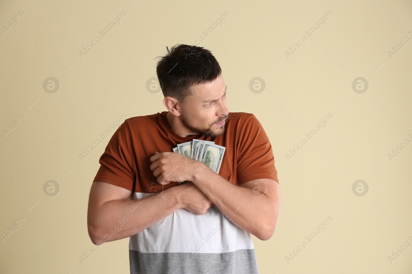 Photo of Greedy man hiding money on beige background