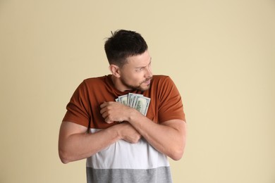 Photo of Greedy man hiding money on beige background
