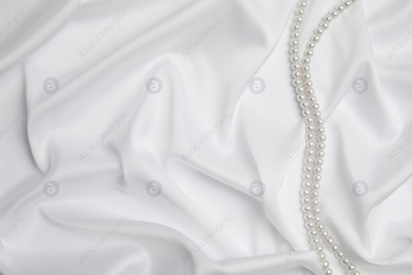 Photo of Beautiful pearls on white silk, top view. Space for text