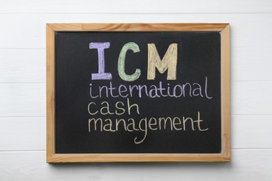 Photo of Small blackboard with abbreviation ICM (International Cash Management) on white wooden background, top view