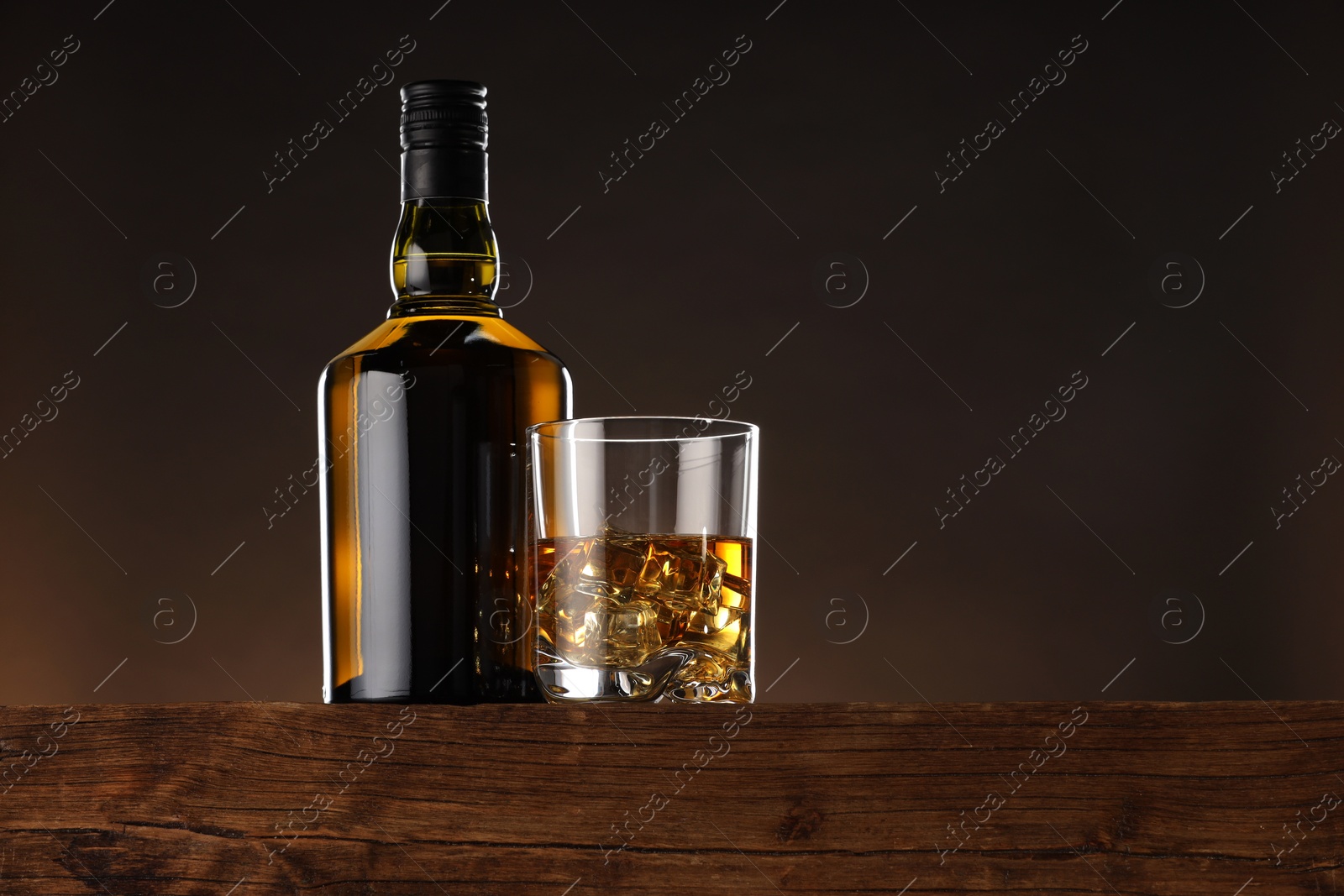 Photo of Whiskey with ice cubes in glass and bottle on wooden table, low angle view. Space for text