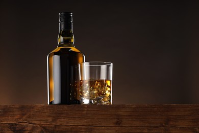 Photo of Whiskey with ice cubes in glass and bottle on wooden table, low angle view. Space for text