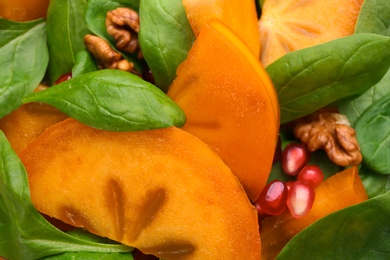 Photo of Delicious persimmon salad with pomegranate and spinach as background, closeup