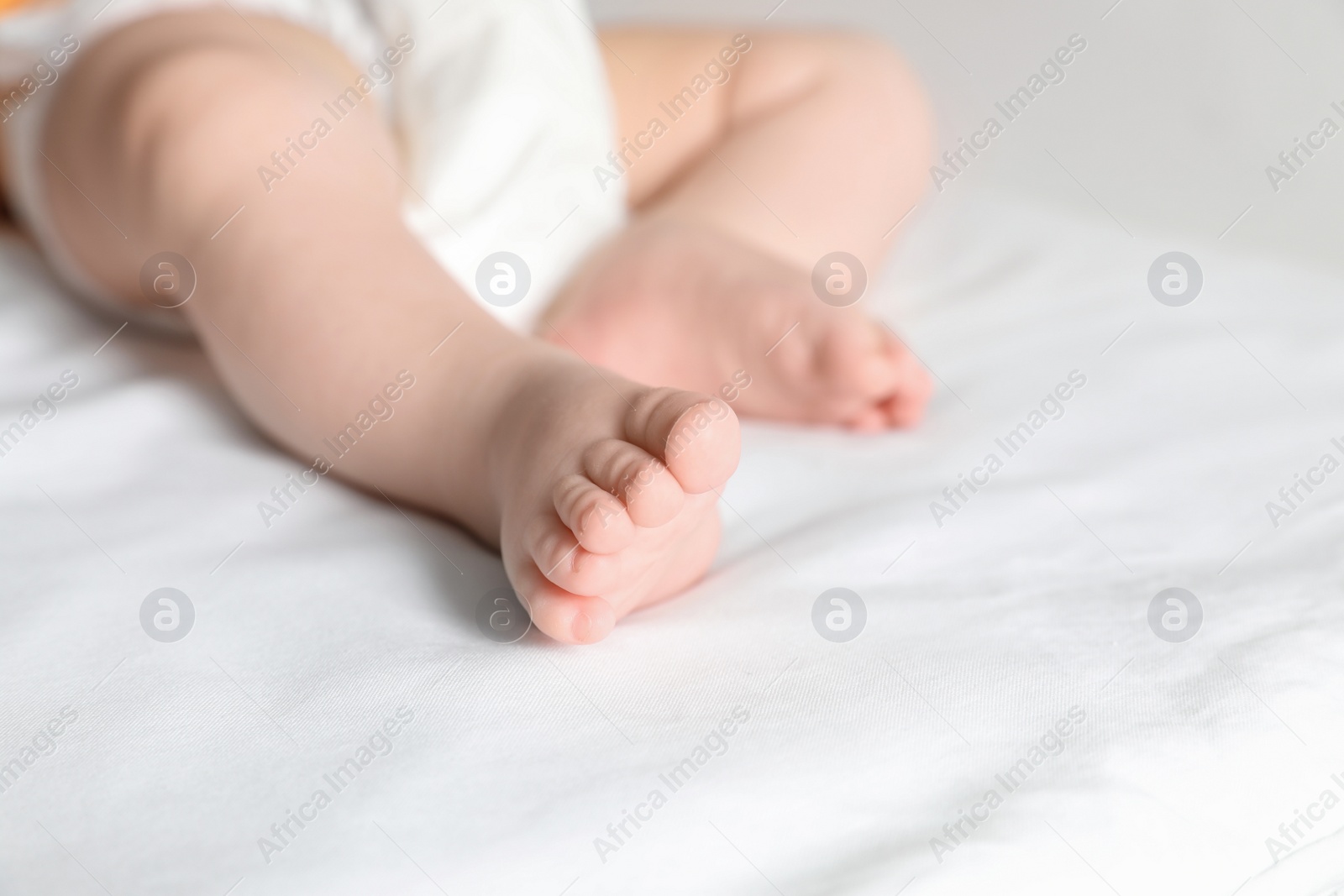 Photo of Little baby with cute feet on bed sheet, closeup. Space for text