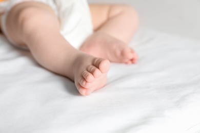 Photo of Little baby with cute feet on bed sheet, closeup. Space for text