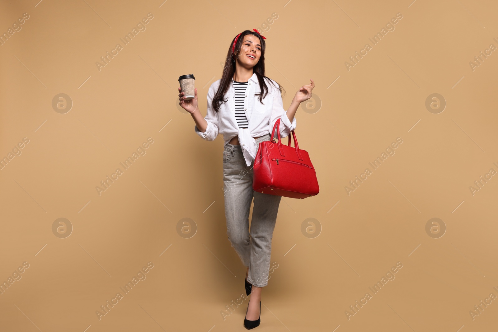 Photo of Young woman with stylish bag and cup of hot drink on beige background