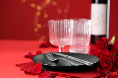 Place setting with roses for romantic dinner on red table, closeup. Space for text