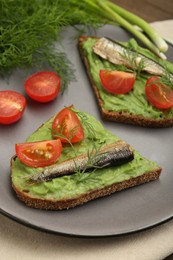 Photo of Delicious sandwiches with sprats, tomatoes, avocado puree and dill on table, closeup