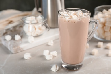 Photo of Tasty hot chocolate with milk and marshmallows in glass cup on table. Space for text