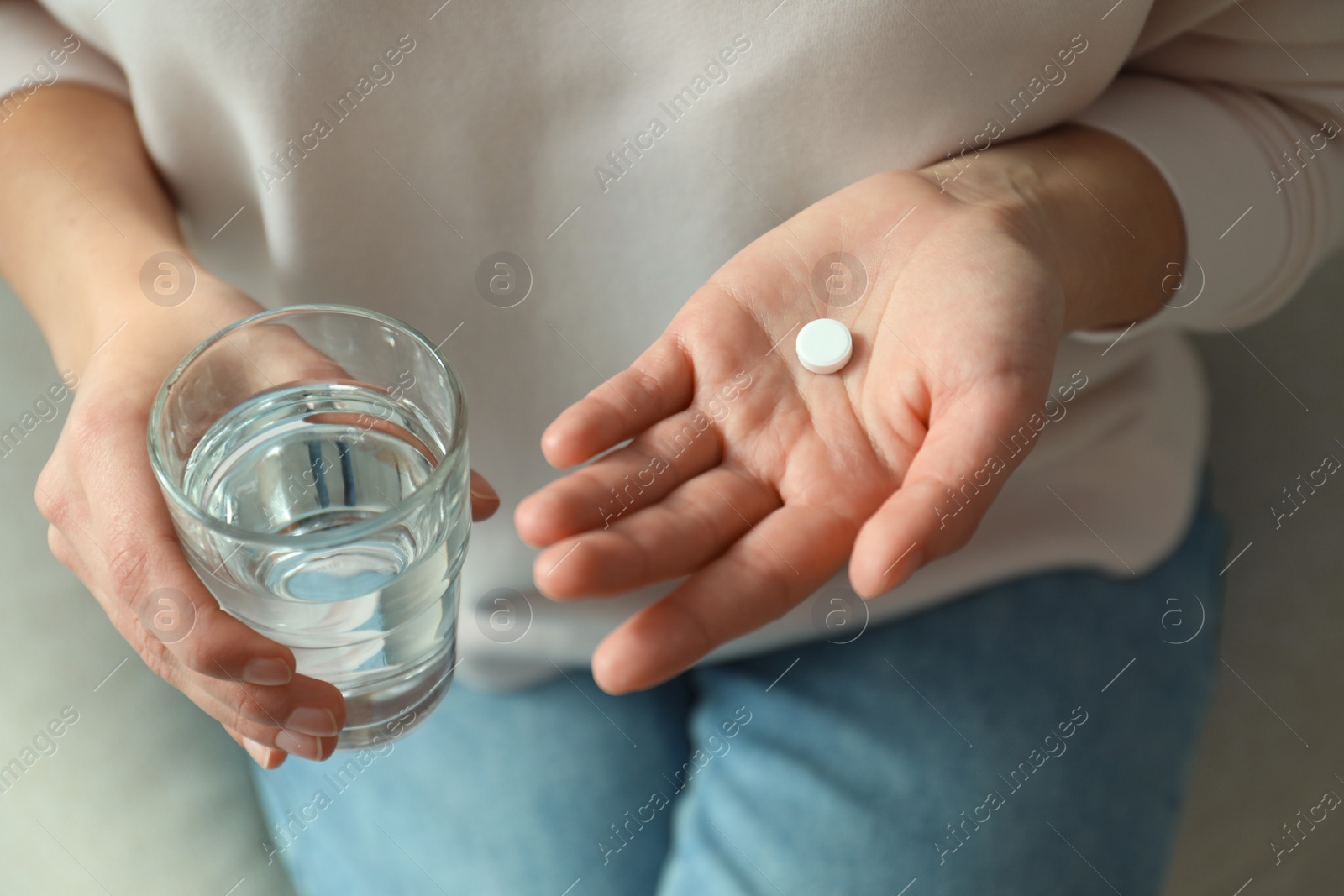 Photo of Young woman with abortion pill and glass of water on sofa, closeup