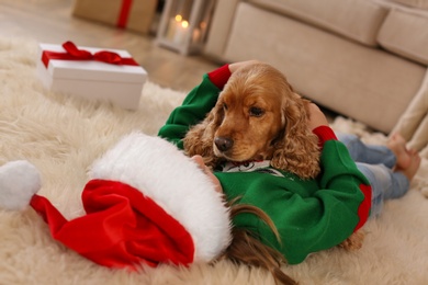 Photo of Cute little child in Christmas outfit with English Cocker Spaniel at home