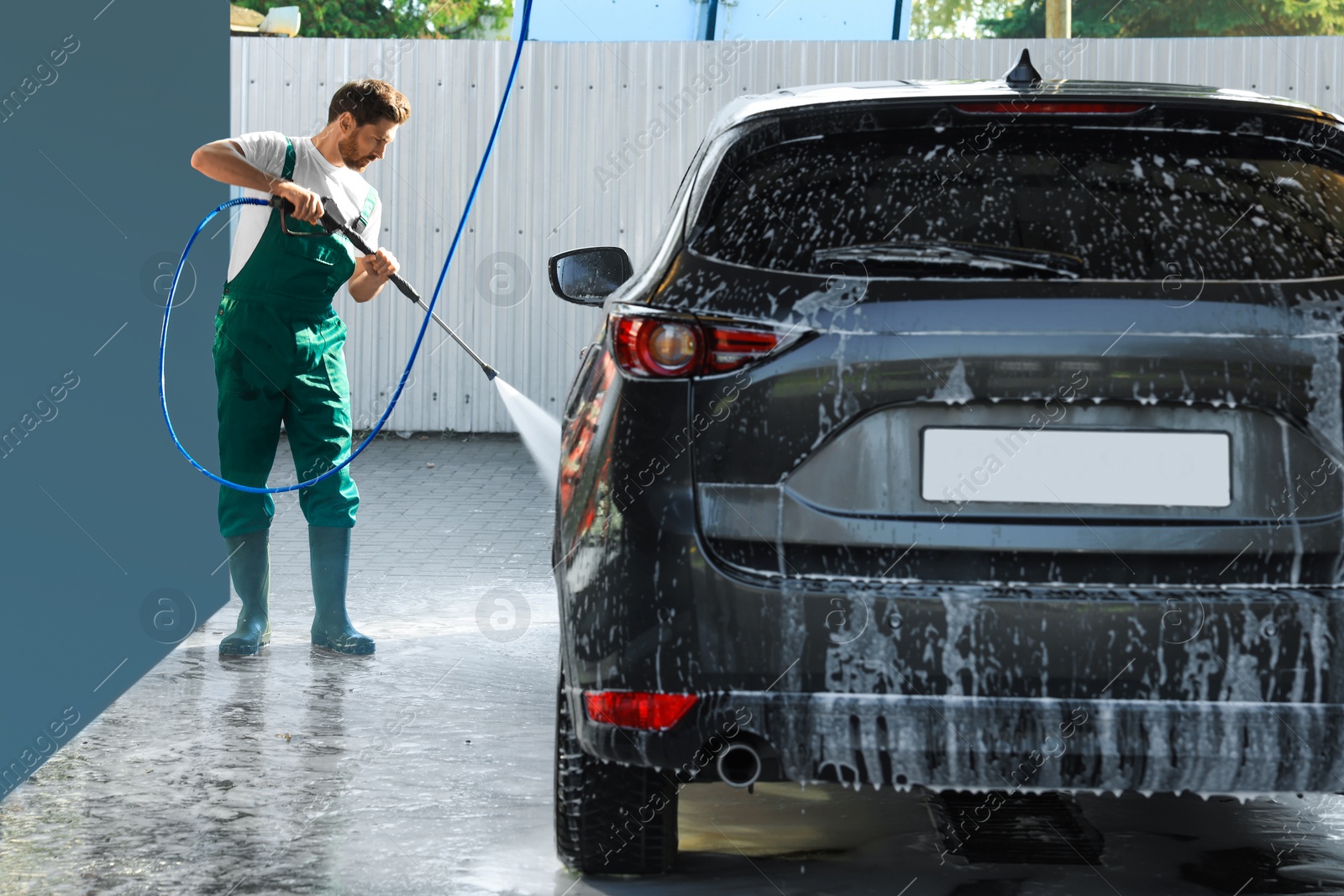 Photo of Worker washing auto with high pressure water jet at outdoor car wash