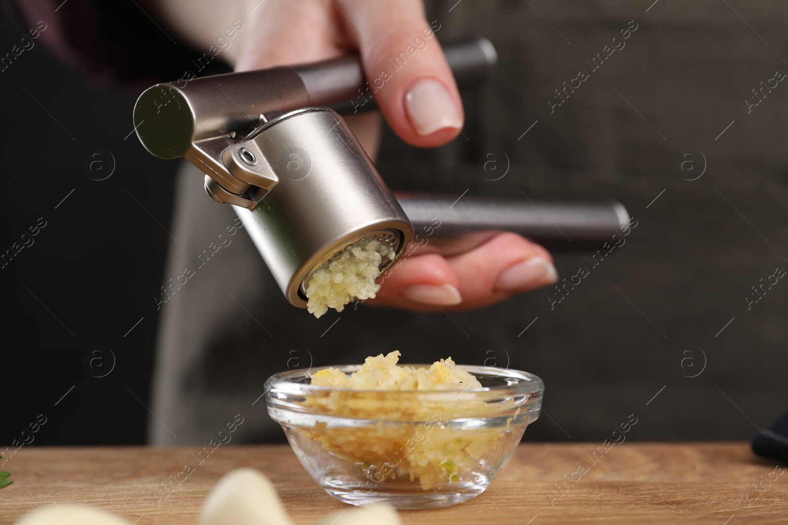 Photo of Woman squeezing garlic with press at wooden table, closeup