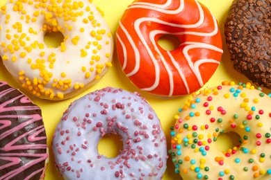 Delicious glazed donuts on yellow background, flat lay