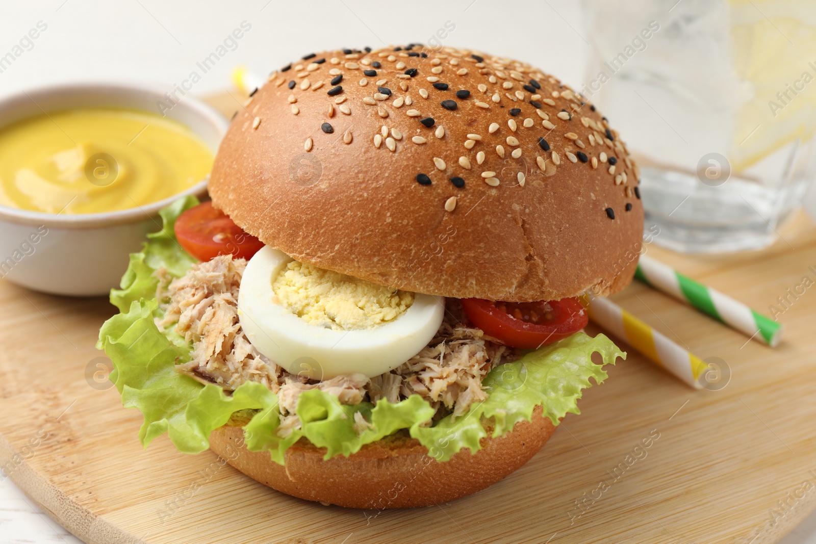 Photo of Delicious sandwich with tuna, boiled egg, vegetables and mustard sauce on wooden board, closeup
