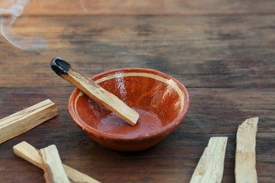 Palo santo stick smoldering in bowl on wooden table