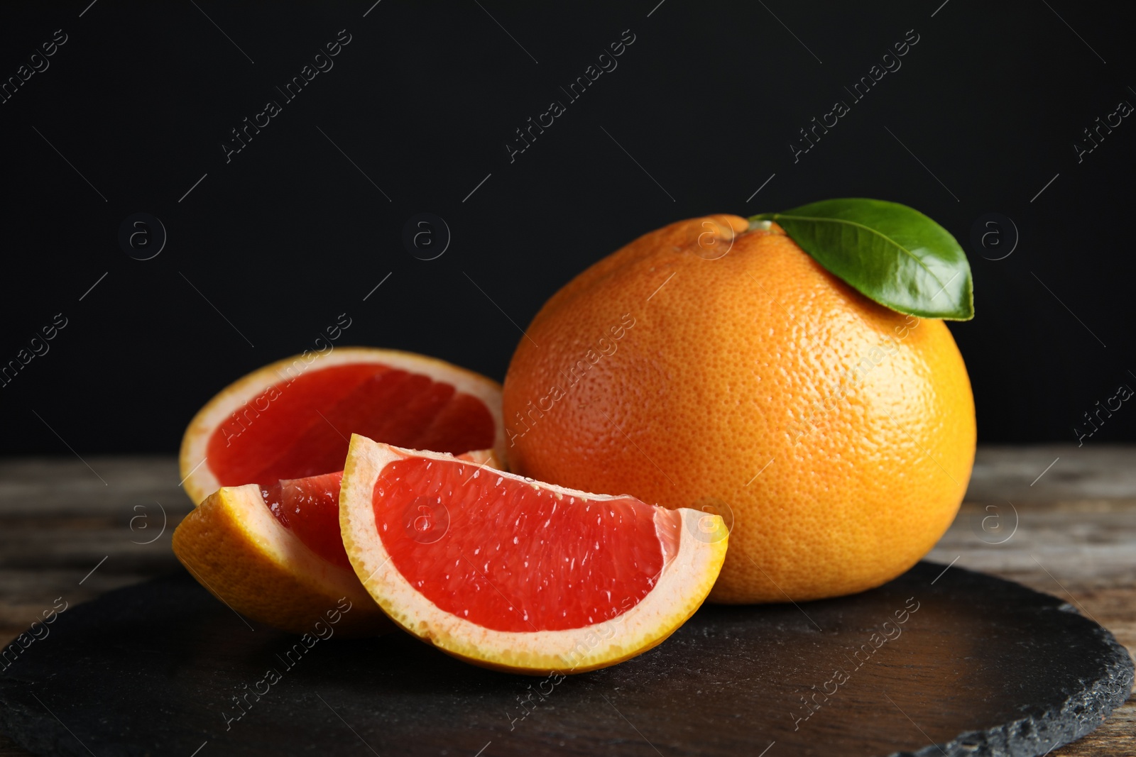 Photo of Fresh tasty grapefruits on slate plate against black background