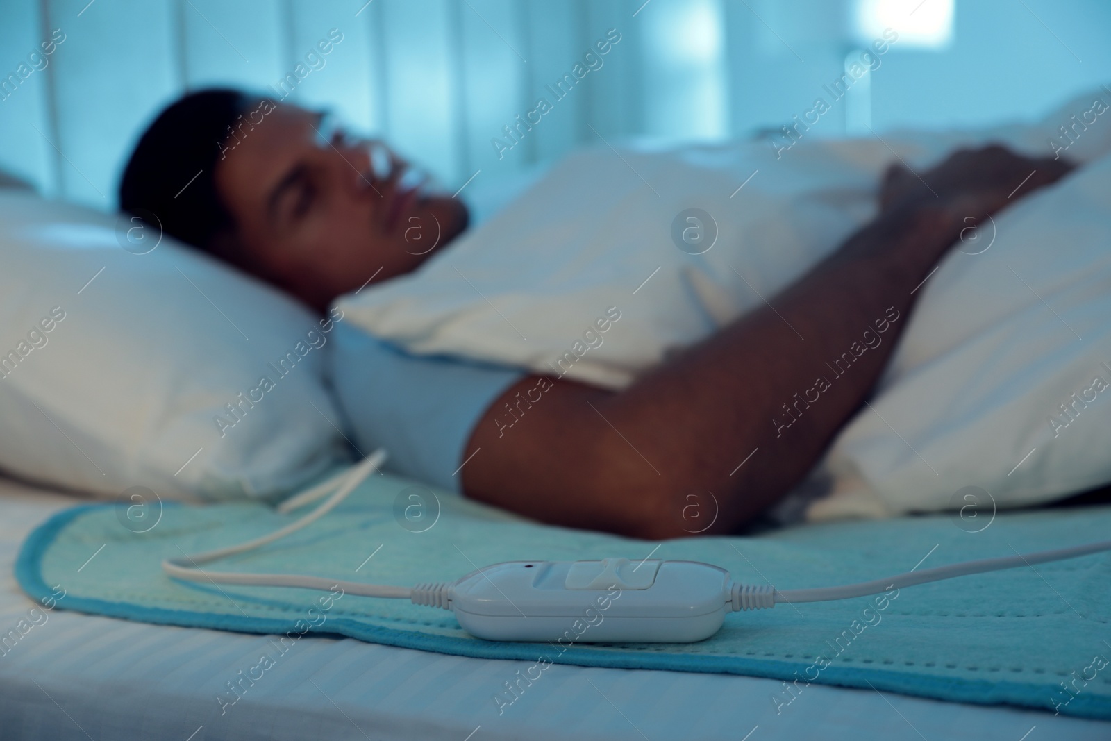 Photo of Man sleeping in bed with electric heating pad, focus on cable