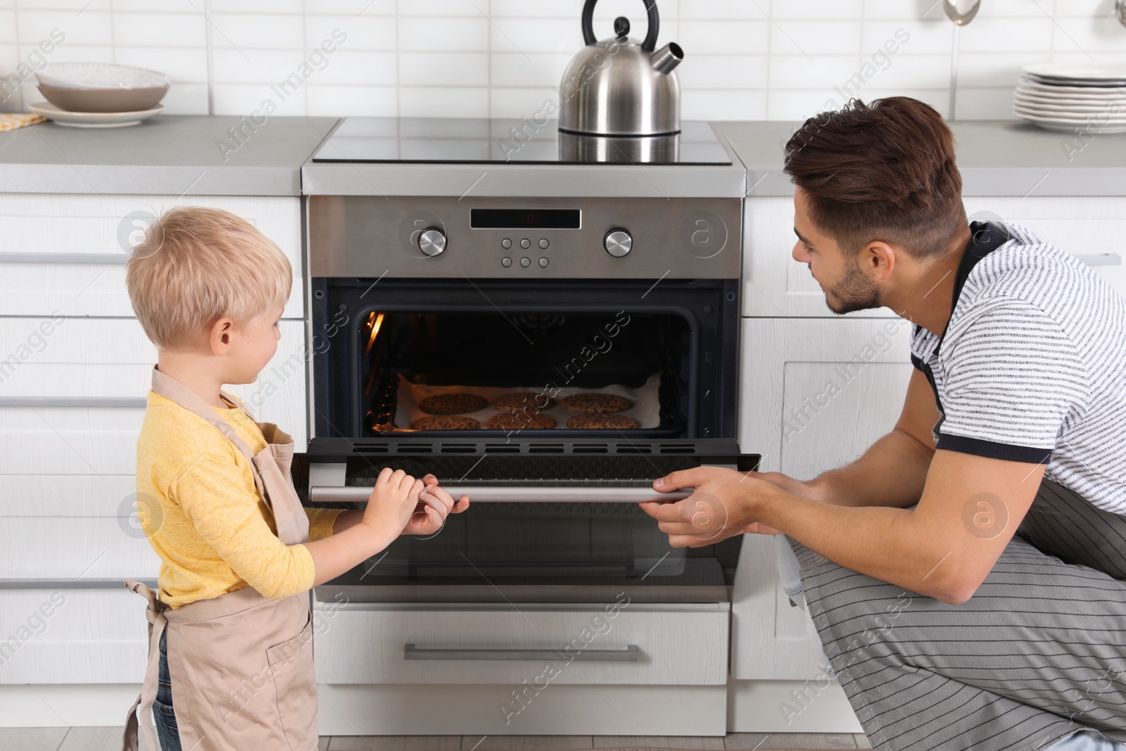 Photo of Young man and his son baking cookies in oven at home